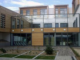 Bâtiment moderne avec une façade vitrée, des accents en bois et une entrée sur cour