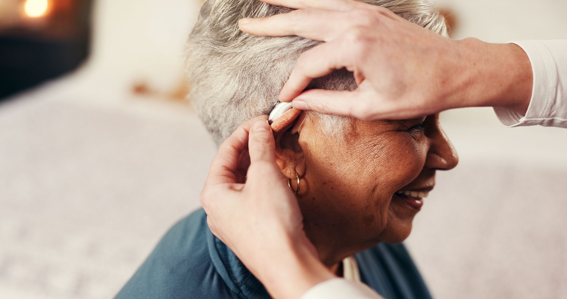 Des mains ajustent un appareil auditif à l'intérieur de l'oreille d'une personne âgée.