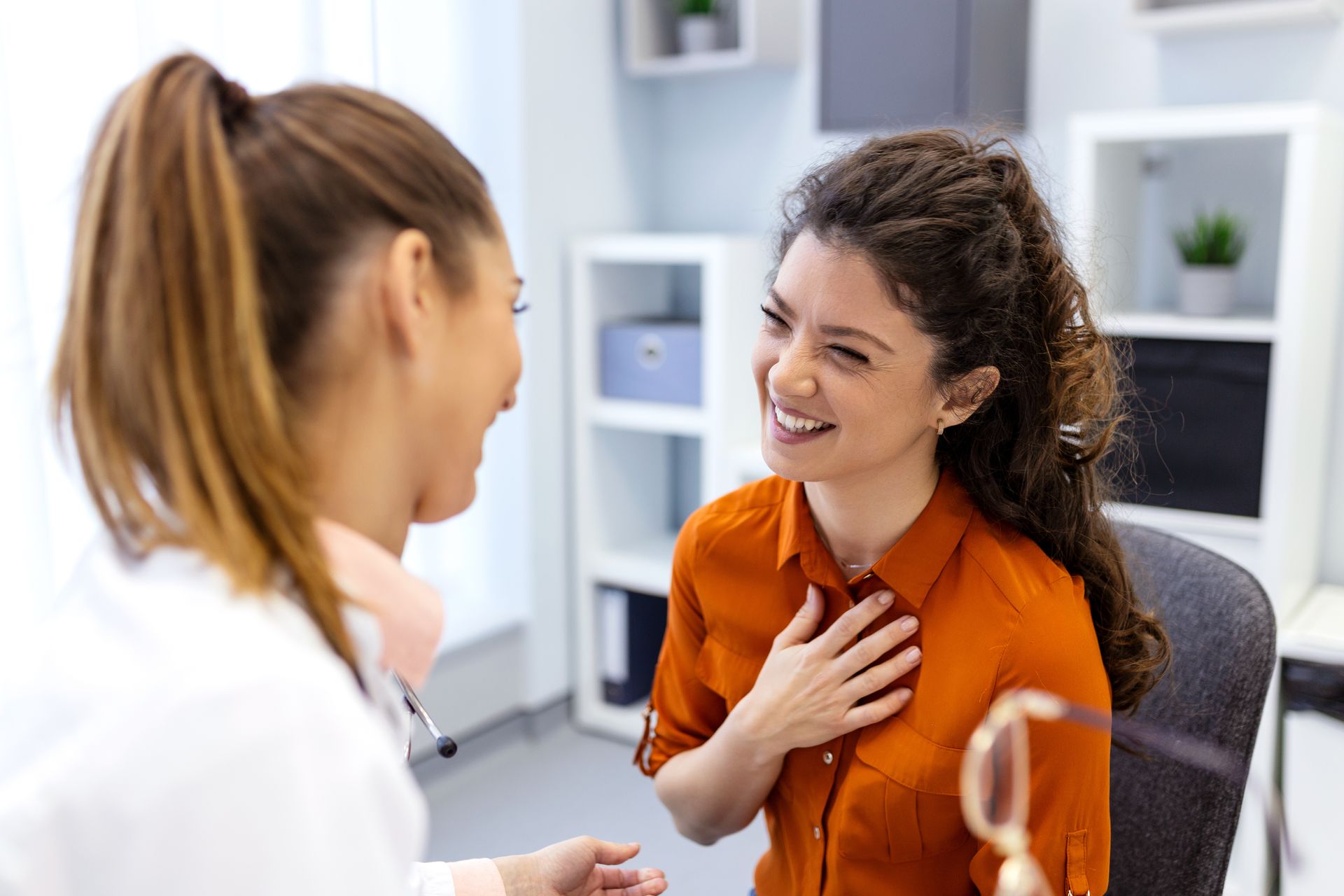 Un médecin parle avec un patient dans un cabinet médical ; le patient sourit, la main sur la poitrine.