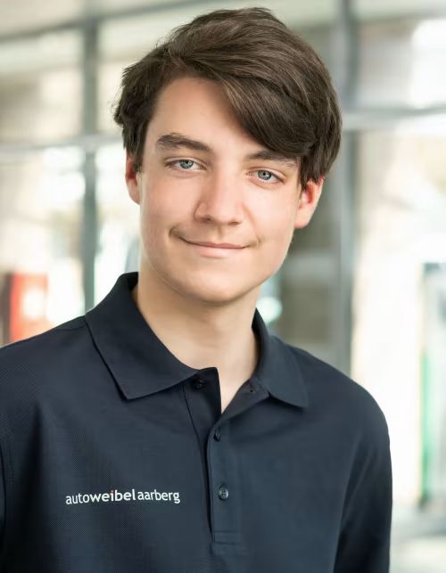 Ein junger Mann in einem schwarzen Poloshirt lächelt in die Kamera.