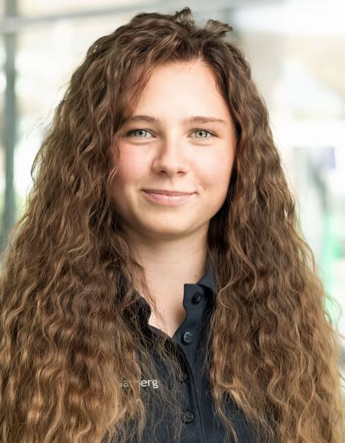 Eine Frau mit langem lockigem Haar trägt ein blaues Hemd und lächelt.