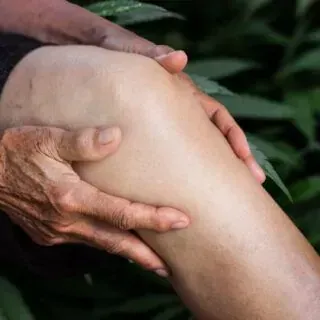 Unas manos sostienen y examinan suavemente la rodilla de una persona.