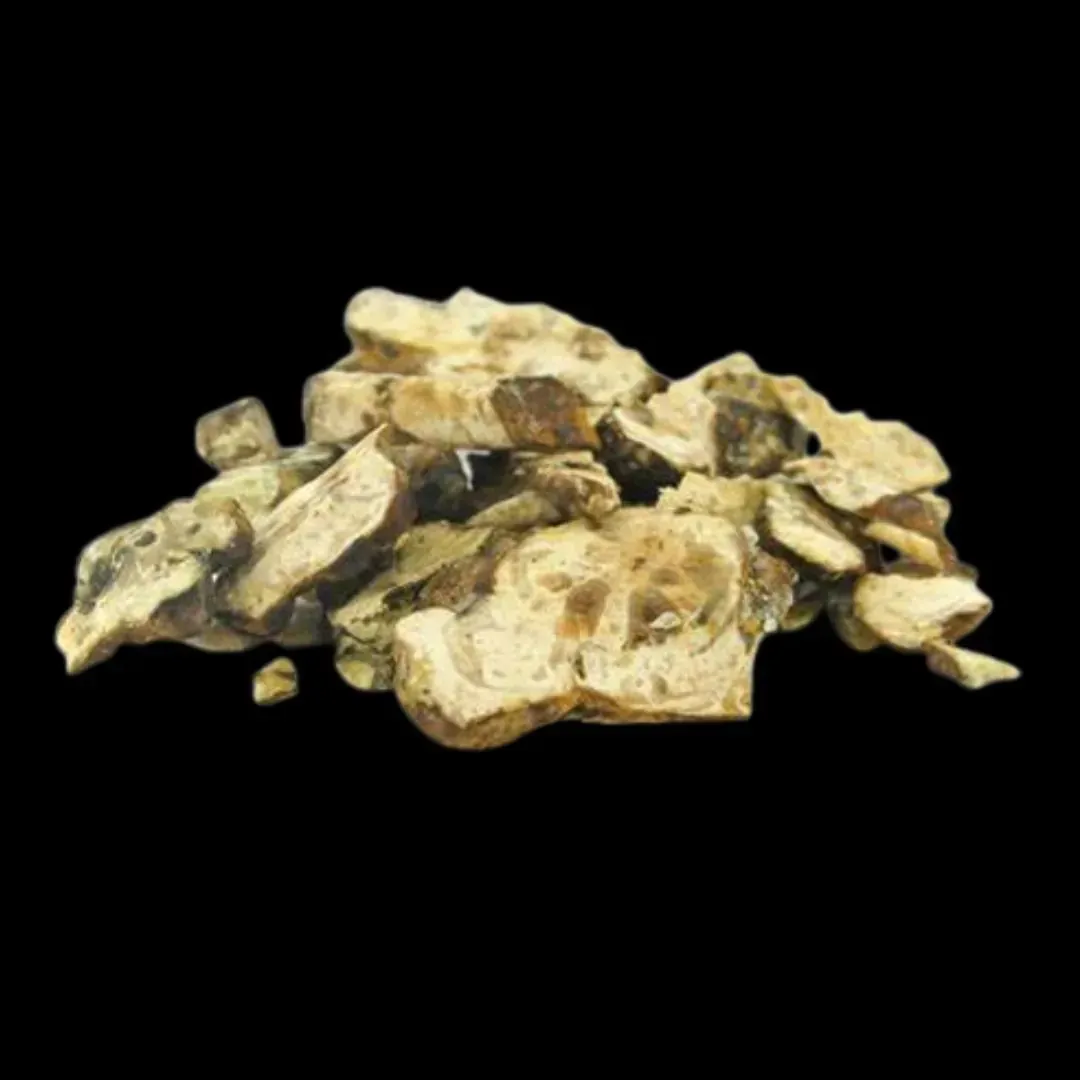 Pila de trozos de jengibre secos, de color marrón claro y tostado, sobre un fondo negro.