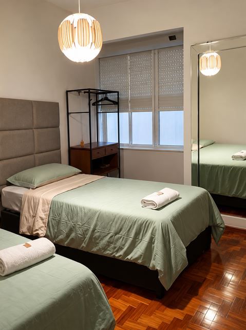 Dormitorio pequeño con dos camas, ropa de cama verde, una ventana y un armario con espejo sobre un suelo de madera