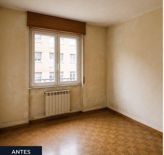 Habitación vacía de color beige con suelo de parquet, una ventana y un radiador debajo