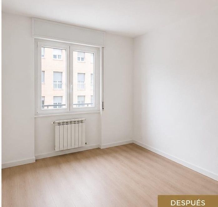 Habitación blanca vacía con una ventana, un radiador y suelo de madera clara