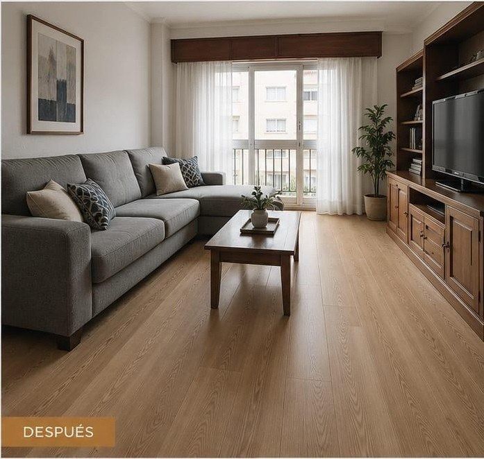 Luminoso y moderno salón con sofá gris, suelo de madera, mesa de centro, televisor y una ventana grande.