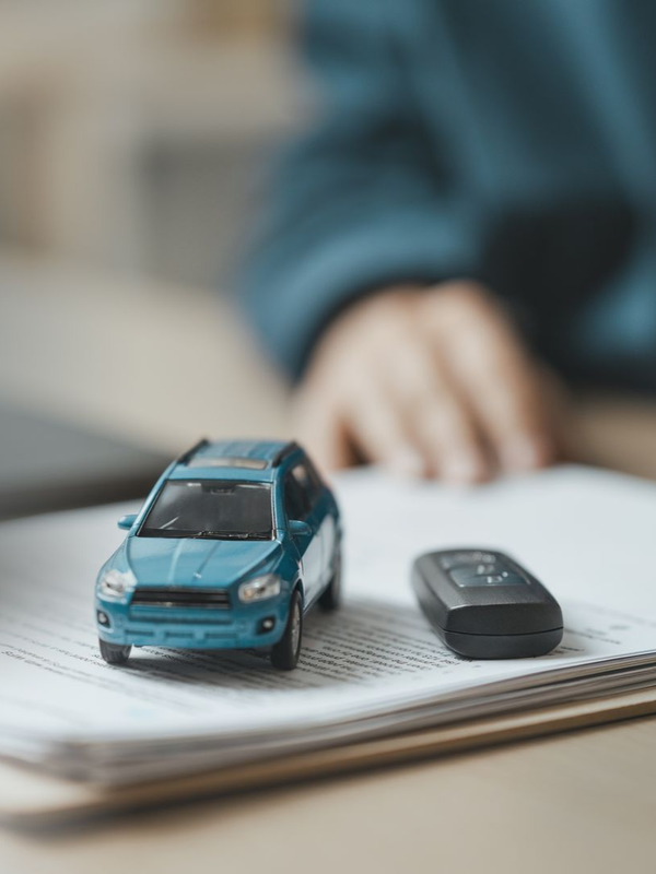 Voiture miniature et porte-clés sur un cahier ouvert, avec une main floue en arrière-plan.