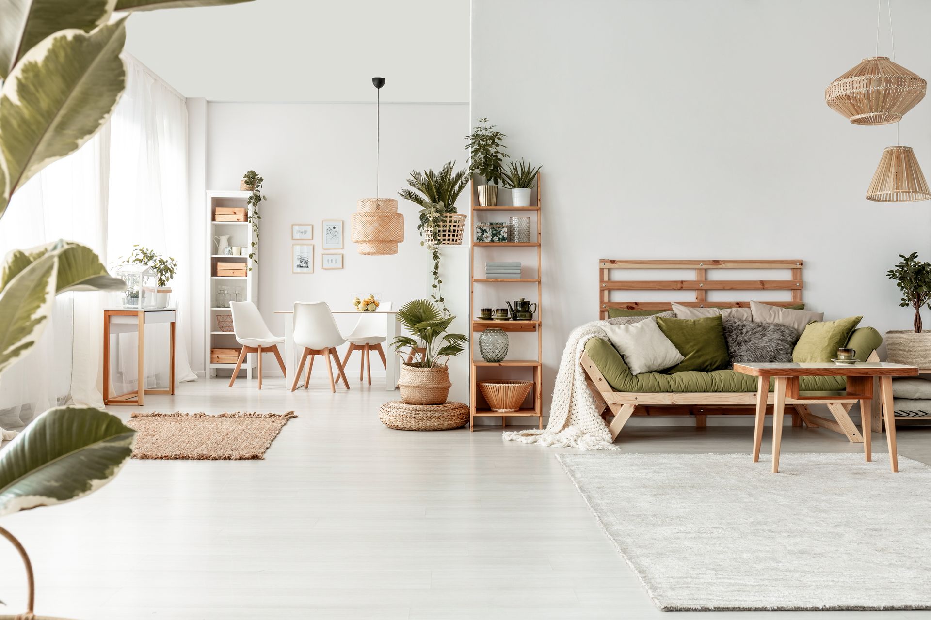 Salon minimaliste et lumineux avec canapé vert, étagères en bois, plantes et murs et sol blancs.