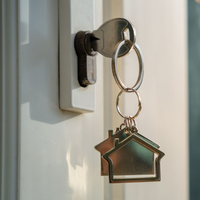 Clé dans la serrure d'une porte avec un porte-clés en forme de maison accroché sur une porte blanche.