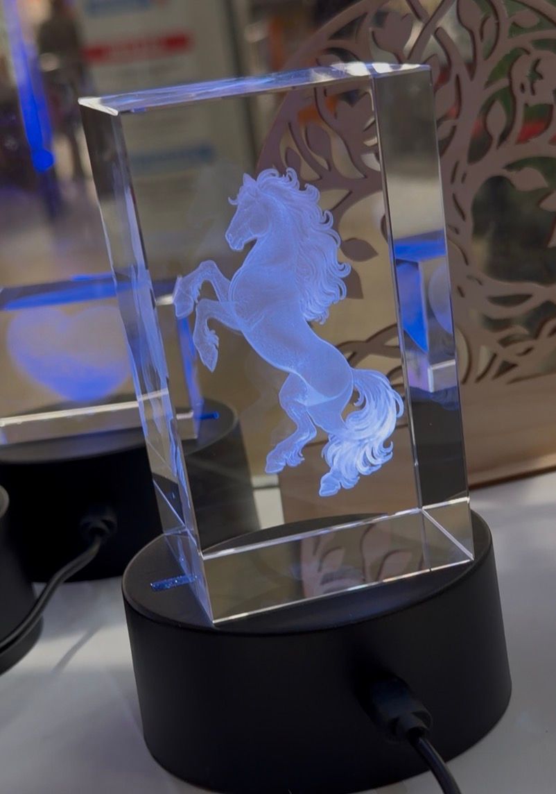 Figurine de cheval en cristal illuminé, sertie dans un bloc transparent sur un socle noir, présentée sur une table