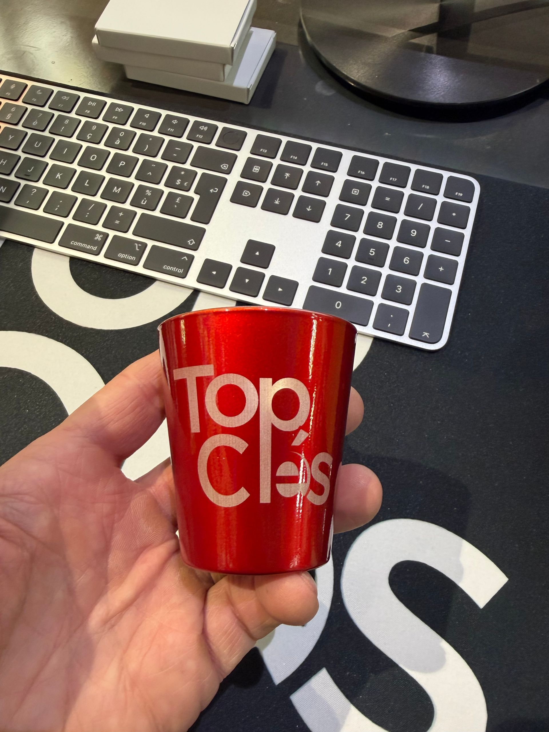 Main tenant une tasse rouge Top Clés devant un clavier sur un bureau