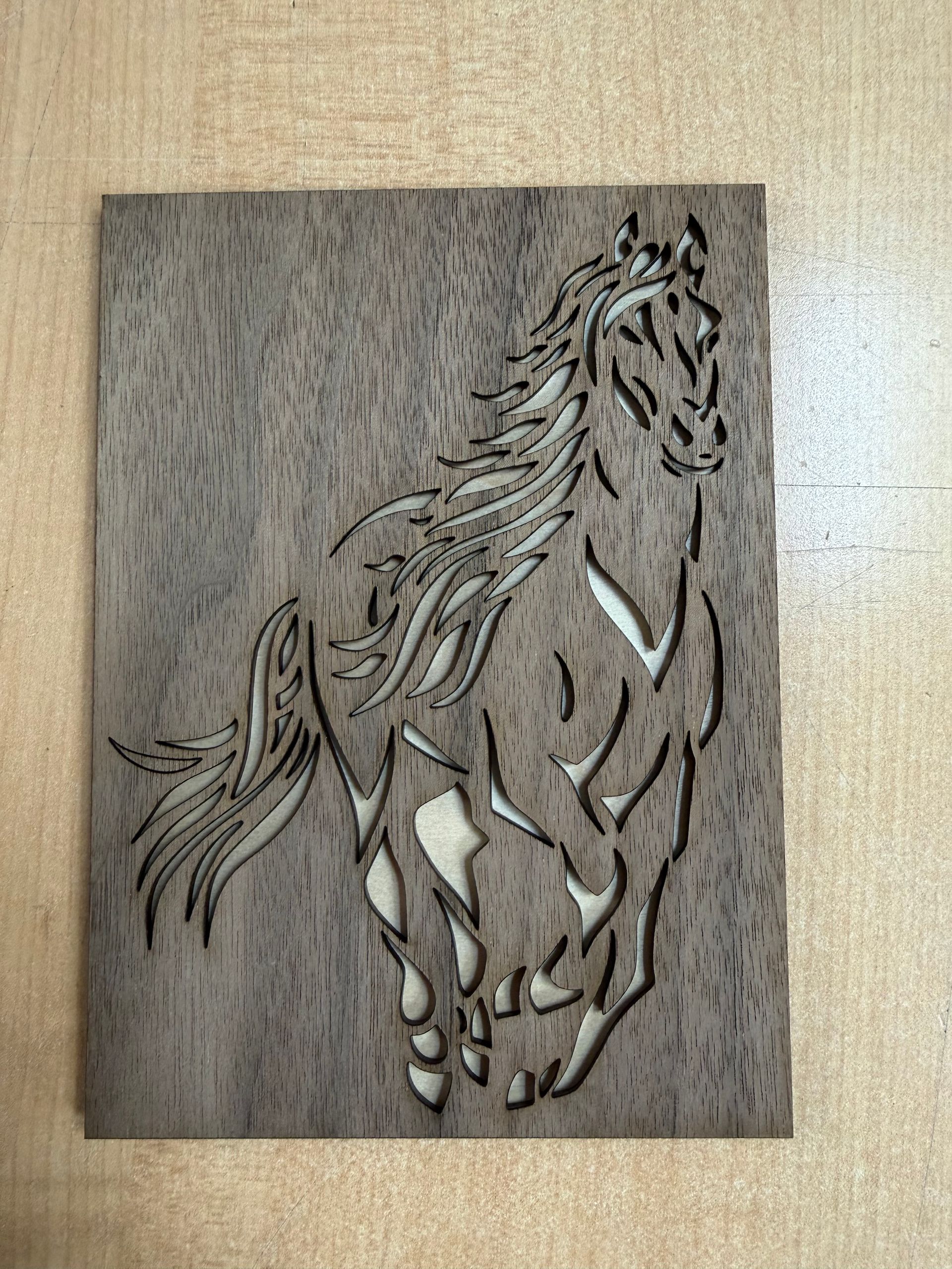 Plaque en bois ornée d'un motif de cheval sculpté en noir et blanc posée sur un table beige.