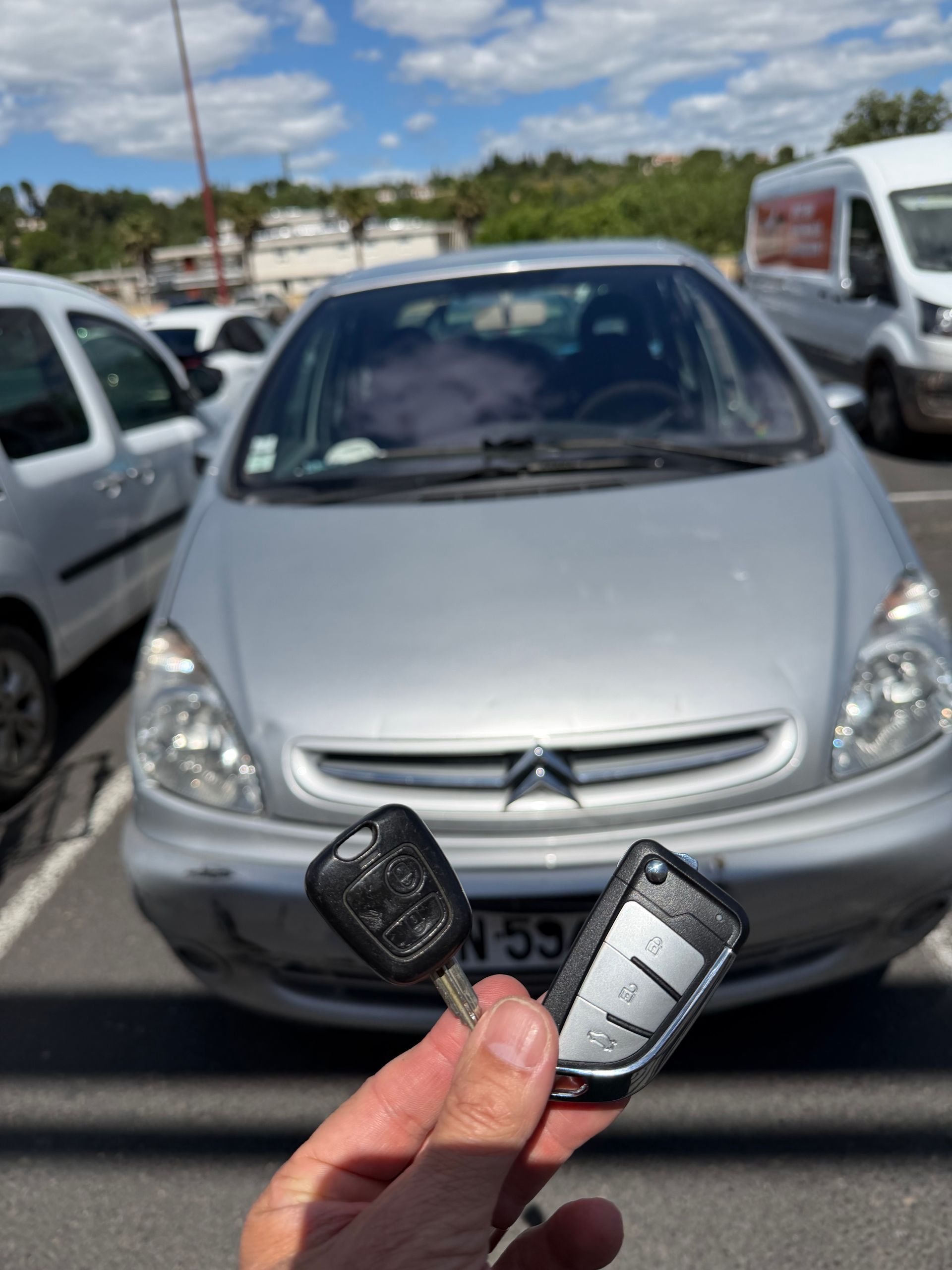 Main tenant une clé de voiture, avec une voiture grise