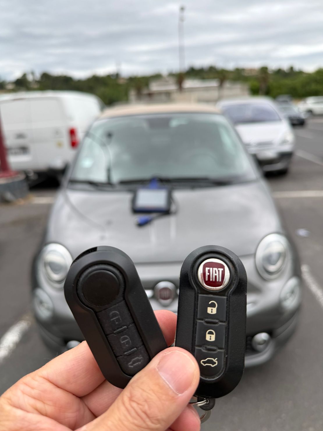 Main tenant une clé de voiture Fiat devant une Fiat grise garée sur un parking
