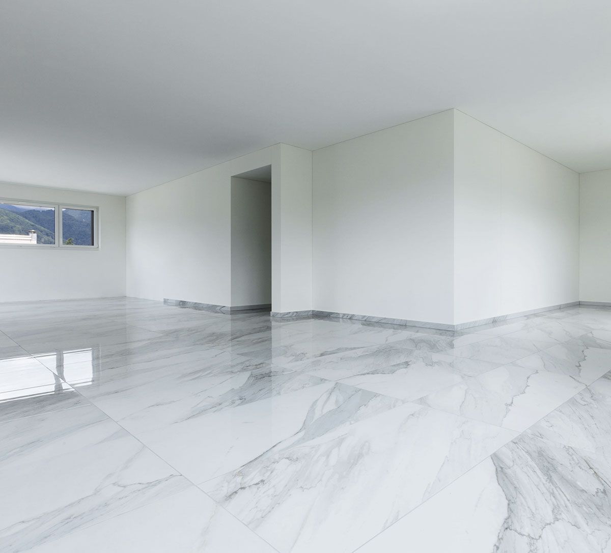 Una habitación interior luminosa y moderna con paredes blancas, suelos de mármol pulido con vetas grises y una ventana con vistas a las montañas.