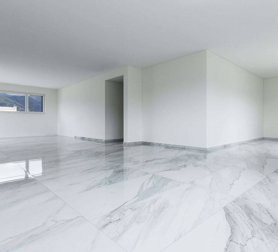 Una habitación interior luminosa y moderna con paredes blancas, suelos de mármol pulido con vetas grises y una ventana con vistas a las montañas.