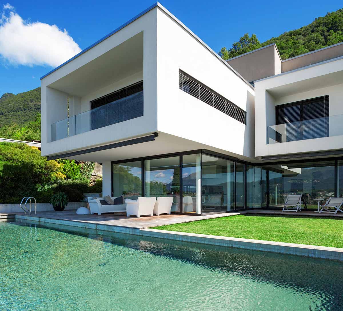 Moderna casa blanca con piscina, paredes de cristal y vistas a la montaña.