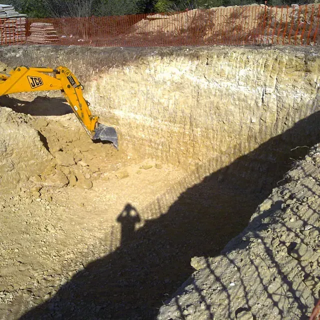 Una excavadora JCB amarilla está cavando un hoyo en la tierra.