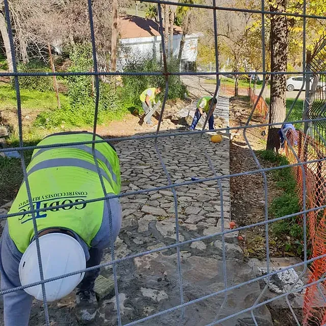 Un hombre con un chaleco amarillo está trabajando en un camino de piedra detrás de una valla.
