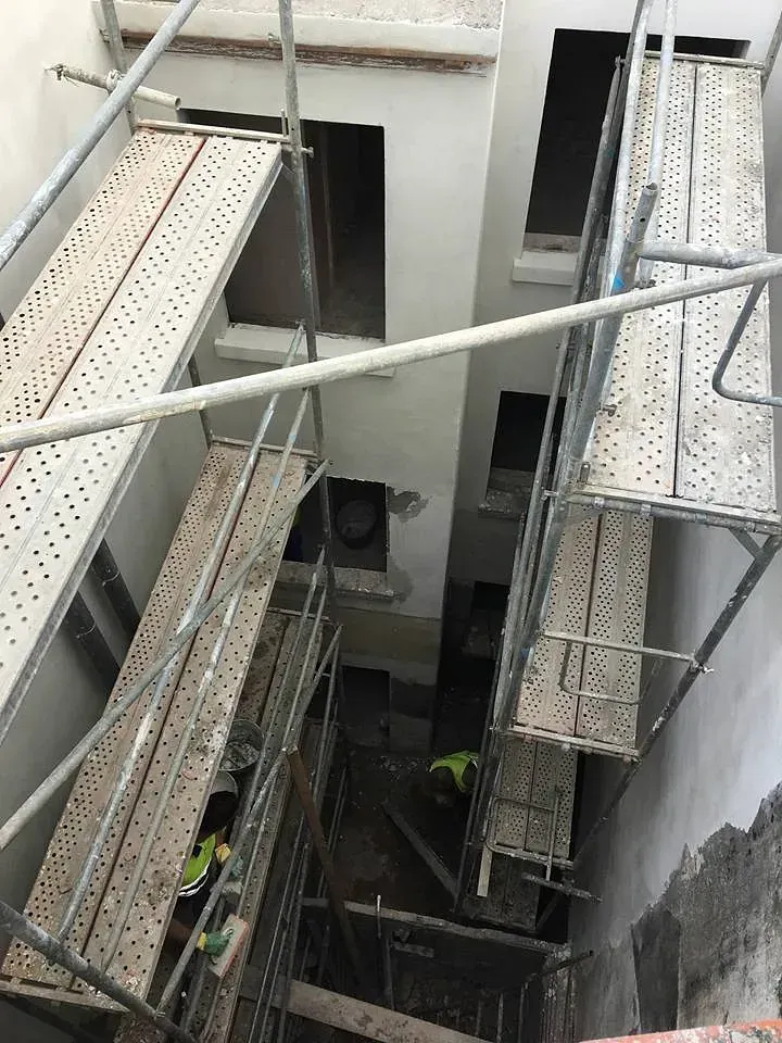Una obra en construcción con andamios y un hombre con un chaleco amarillo.