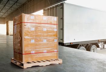 Palet de cajas empaquetadas envueltas en plástico en un muelle de carga, al lado de un camión semirremolque.