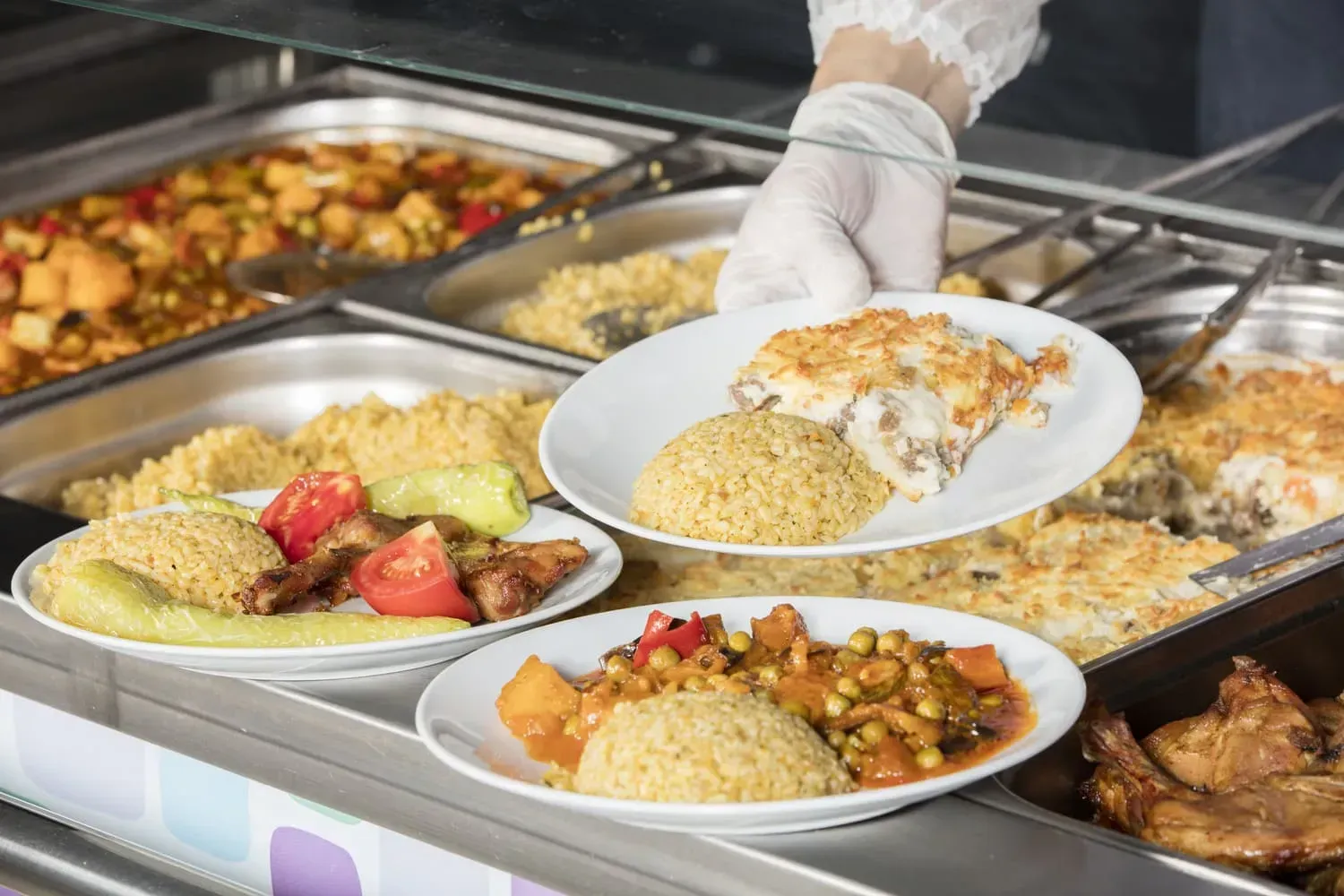 Una persona está tomando un plato de comida de una línea de buffet.