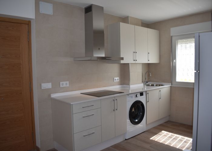 Una cocina con gabinetes blancos y lavadora y secadora.