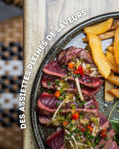 Plat composé de viande saisie en tranches, de frites et d’une garniture aux herbes, présenté sur une assiette sombre