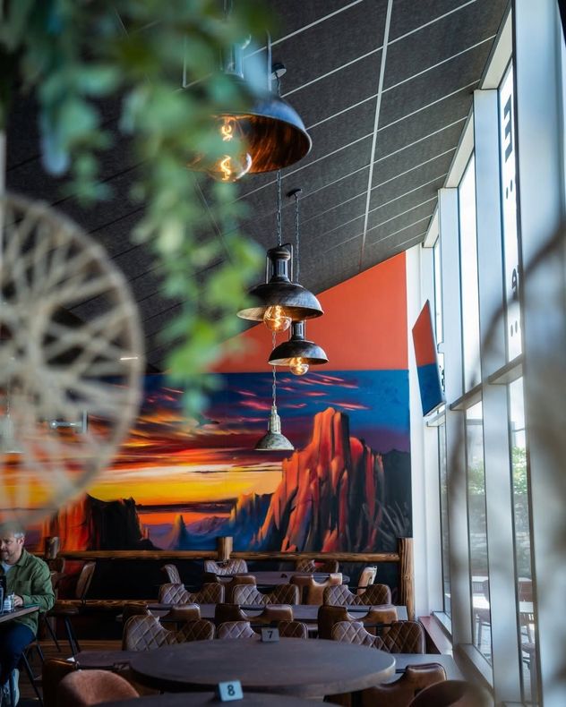 Terrasse de restaurant moderne, ornée de suspensions en cuivre et d’une fresque représentant un coucher de soleil aux couleurs vives