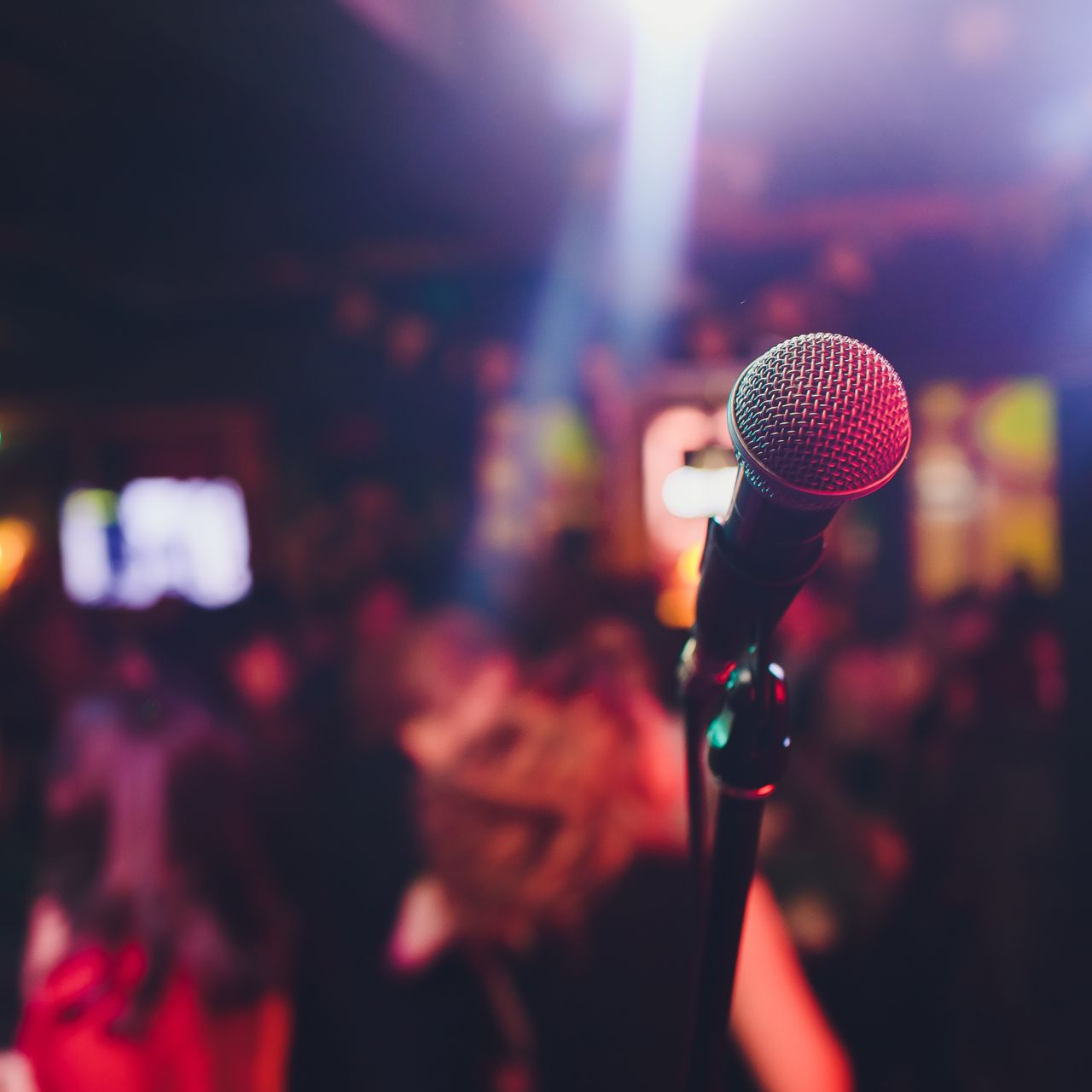 Microphone sur scène, avec une foule floue et des lumières colorées en arrière-plan