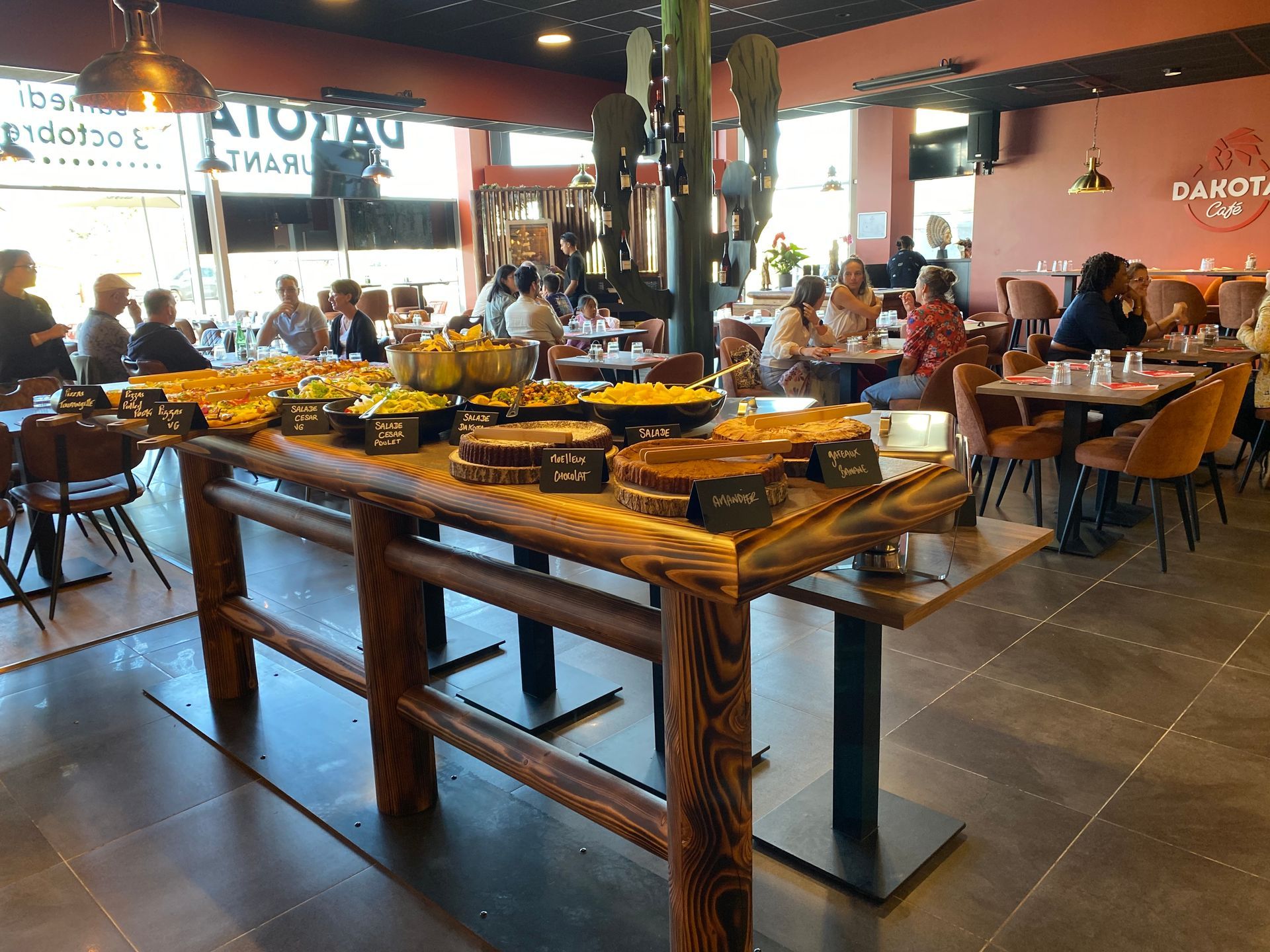 Buffet de restaurant intérieur avec des tables en bois, de la vaisselle jaune et des clients assis à l’arrière-plan