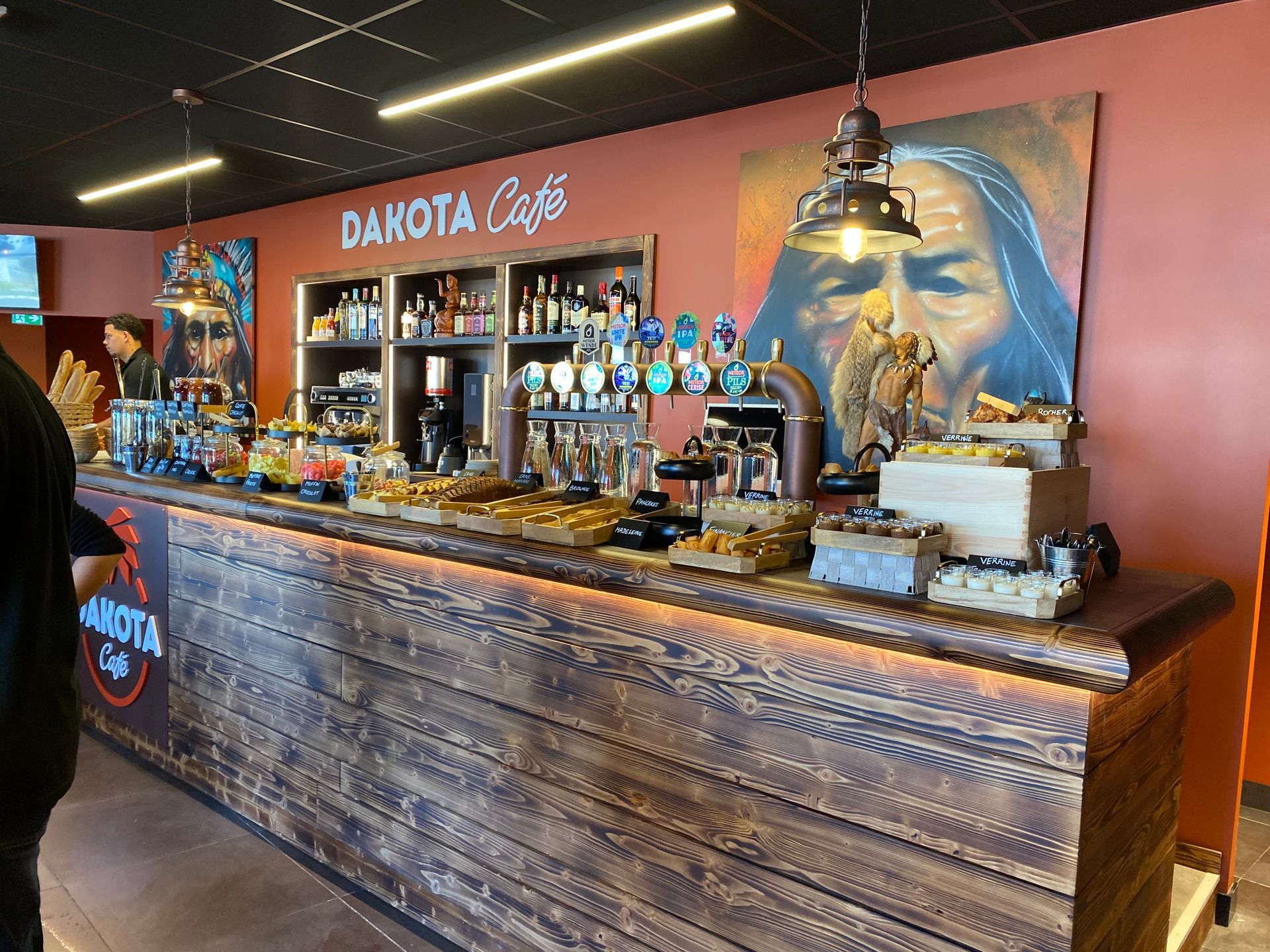 Bar du Dakota Café avec comptoir en bois rustique, tireuses à bière et fresque bleue derrière le comptoir
