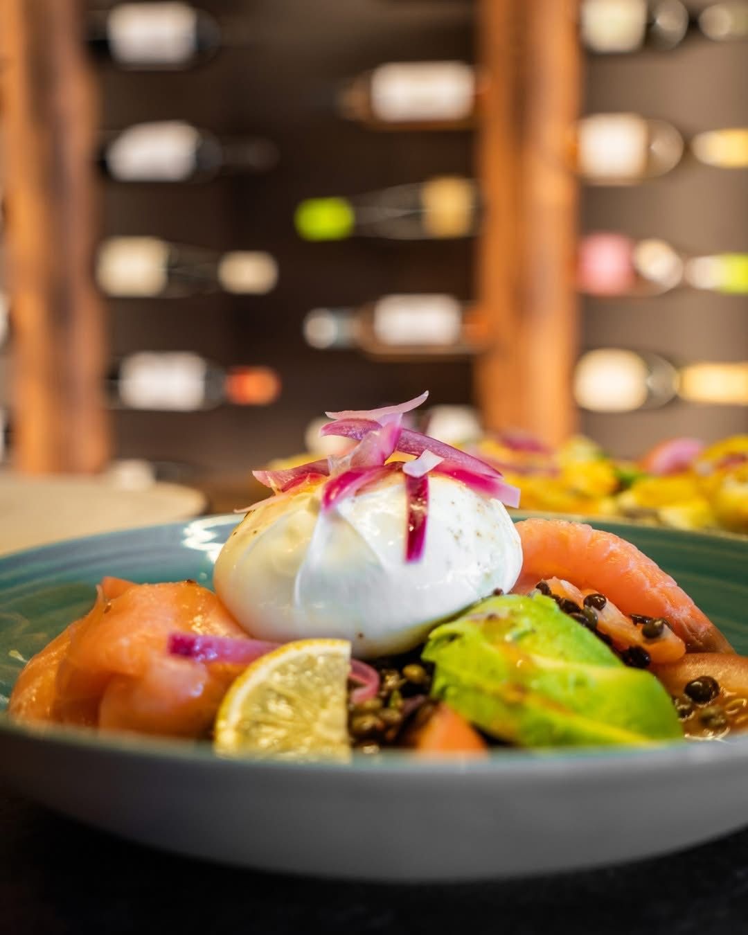 Bol gastronomique avec une boule de burrata, des fruits colorés et des fleurs, posé sur une table de restaurant