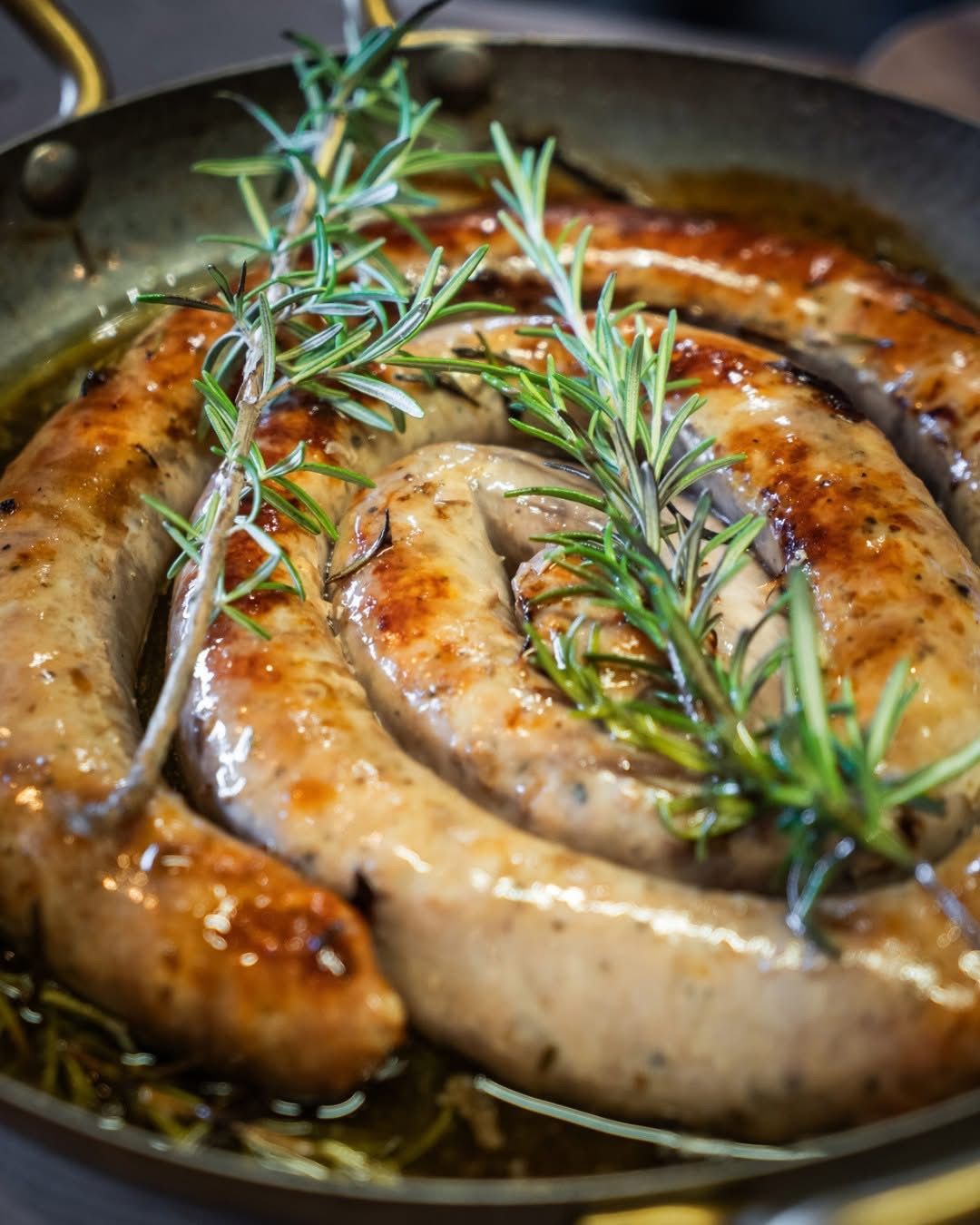 Des saucisses en spirale qui grésillent dans une poêle, garnies de brins de romarin