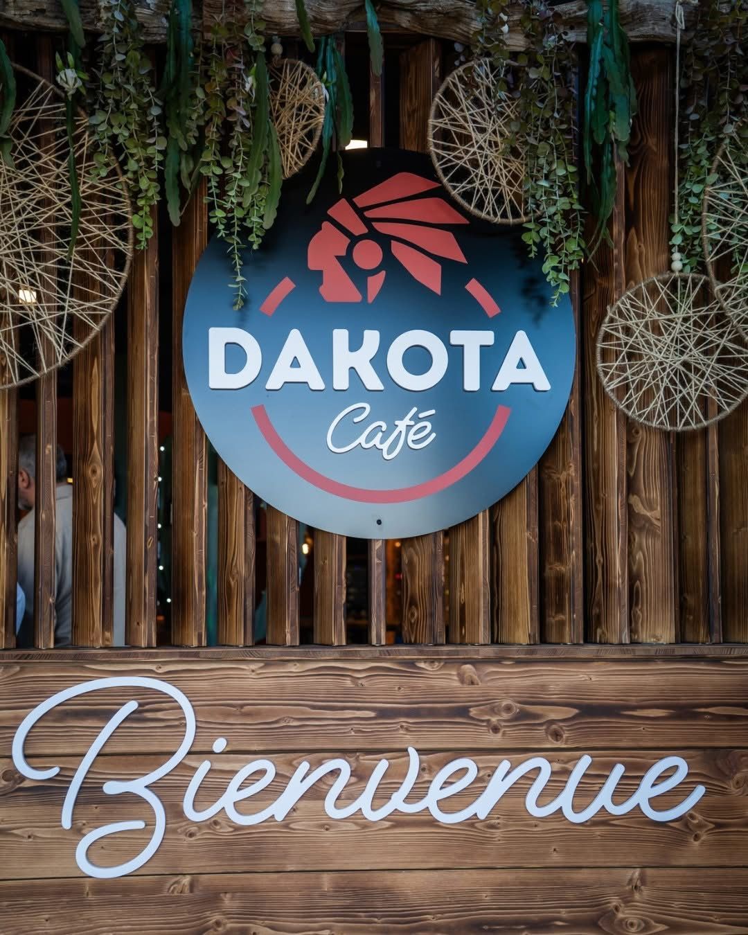 Enseigne Dakota Café au-dessus d’un mur en bois décoré de suspensions, avec le mot « Bienvenue » en dessous