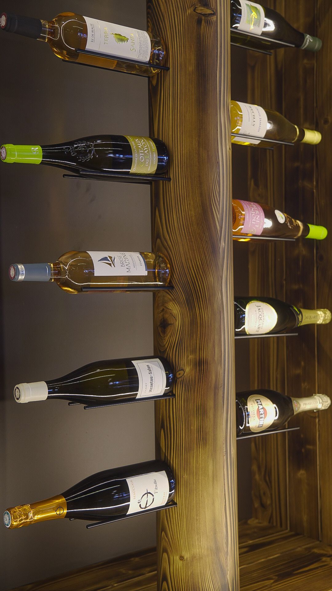 Bouteilles de vin exposées sur des casiers en bois dans une cave, vues à la verticale.