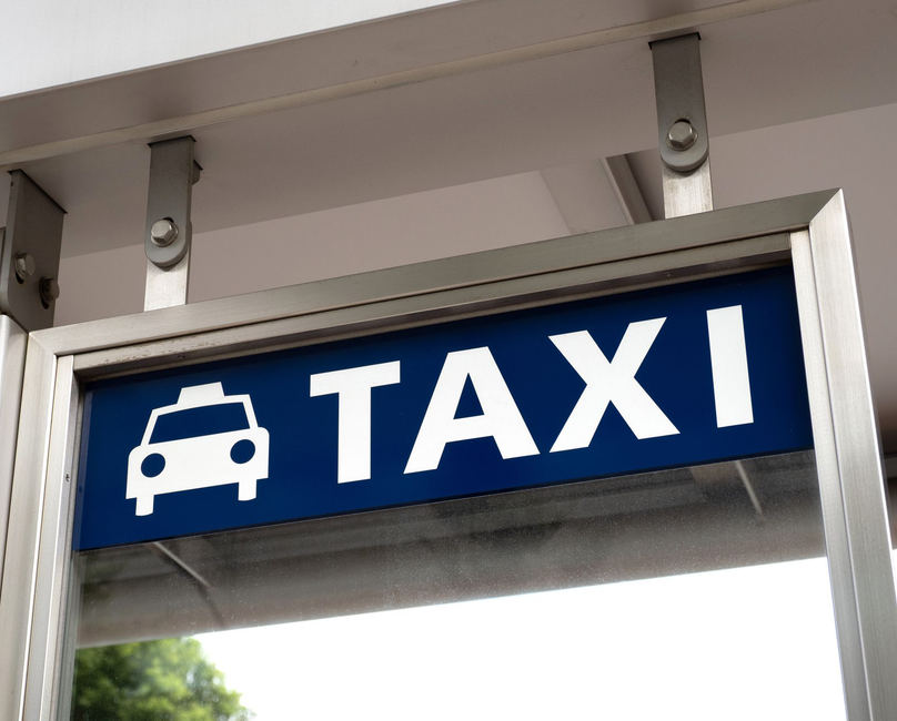 Panneau de taxi avec texte blanc et symbole de voiture sur fond bleu, dans un cadre métallique.
