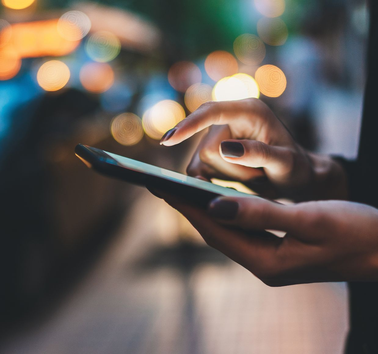 Main tenant un téléphone allumé, doigt tapotant l'écran. Arrière-plan flou.