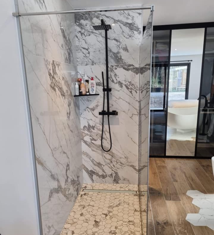 Douche moderne avec carrelage imitation marbre, robinetterie noire, paroi de douche en verre.