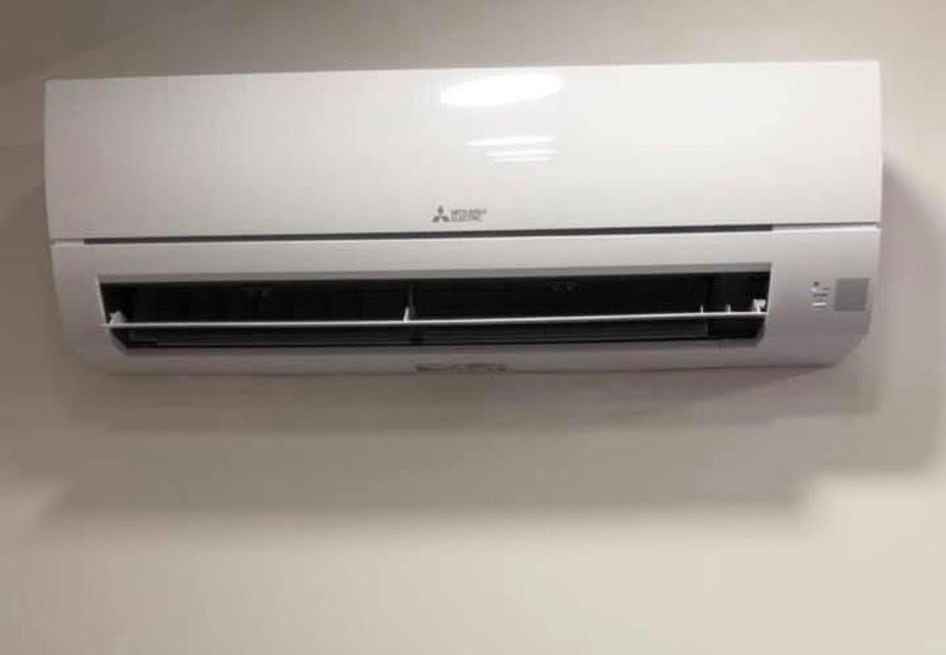 Climatiseur Mitsubishi blanc fixé sur un mur beige.