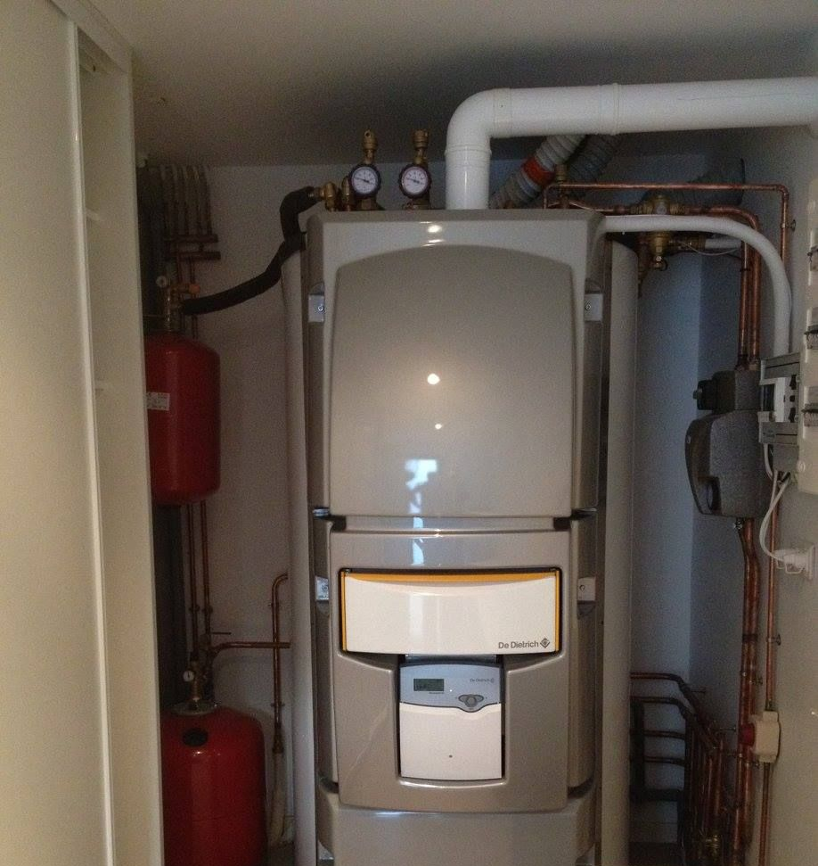 Chauffe-eau de grande taille, de couleur argentée, avec réservoirs rouges et tuyaux en cuivre, installé dans un local technique fermé.