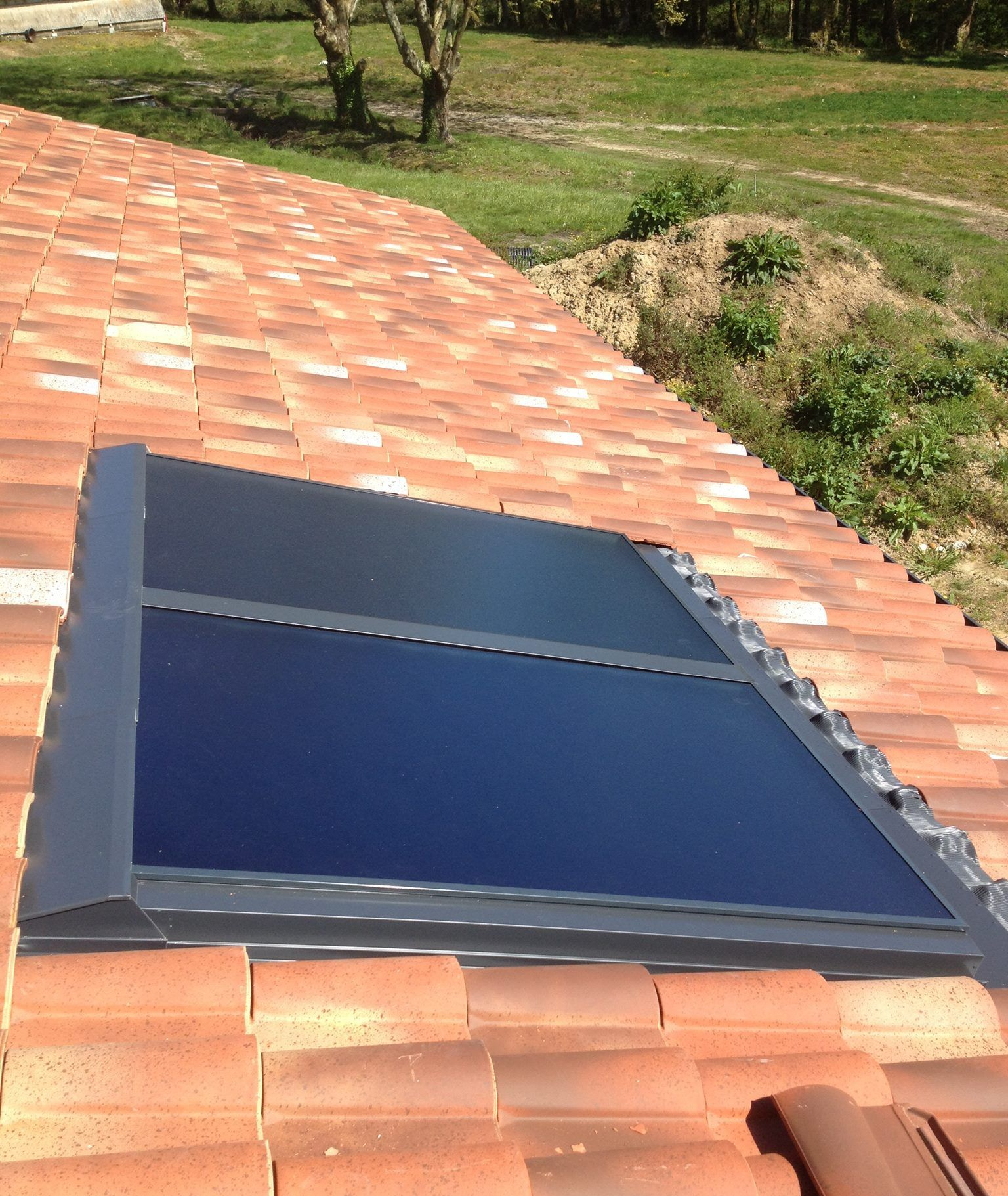 Des panneaux solaires installés sur un toit de tuiles en terre cuite reflètent le ciel.