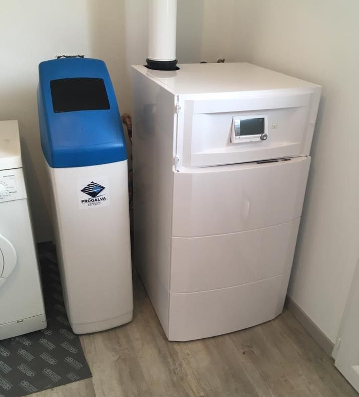 Adoucisseur d'eau et chaudière dans une buanderie ; appareils électroménagers bleus et blancs à côté d'une machine à laver.