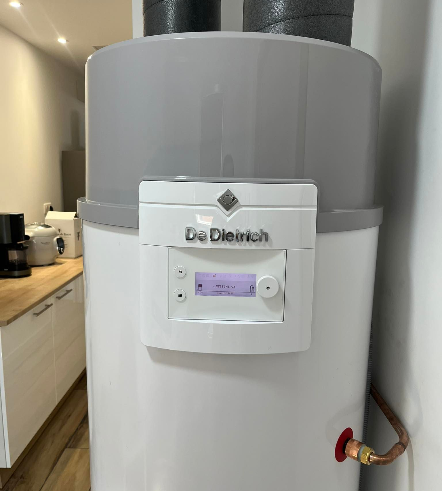 Chauffe-eau mural blanc avec affichage numérique et tuyauterie de raccordement.