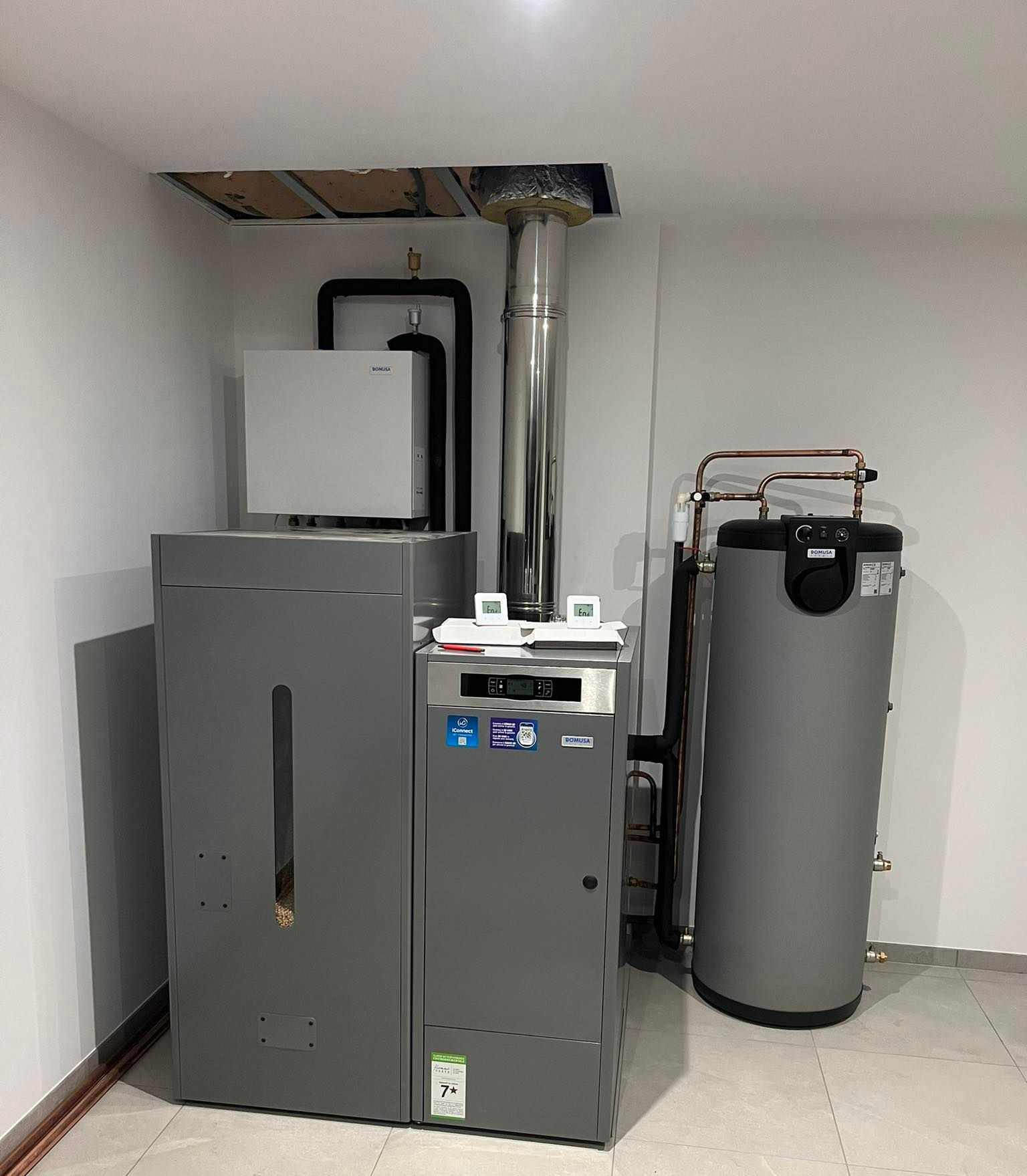 Un système de chaudière à granulés gris dans une buanderie, avec un réservoir d'eau chaude et une ventilation.