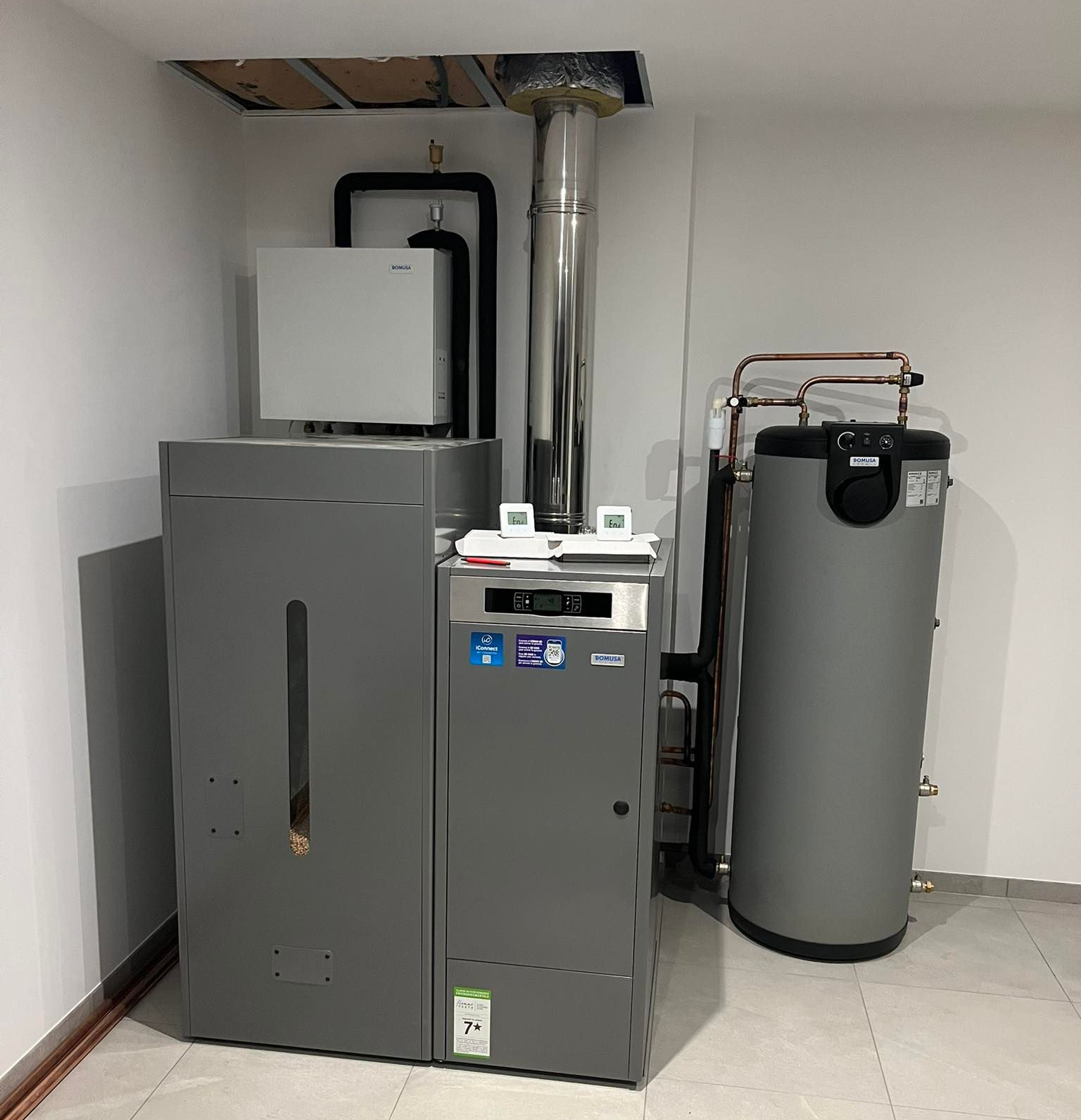 Une chaudière grise, un chauffe-eau et les composants qui y sont raccordés dans une buanderie.