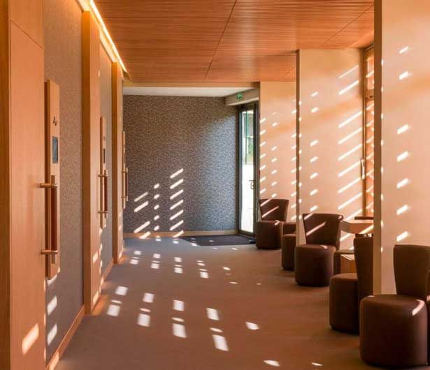 Couloir moderne avec plafond en bois chaleureux, motifs de lumière du soleil au sol et chaises sombres le long du mur