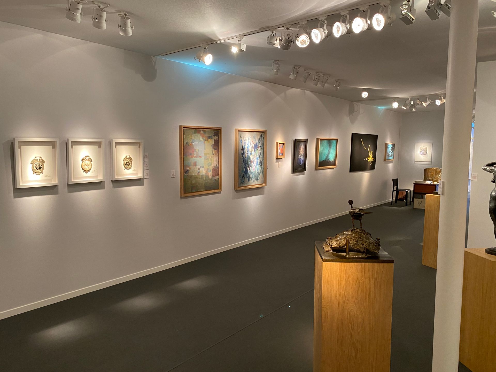 Salle d'une galerie d'art avec des tableaux et des sculptures sur des supports en bois
