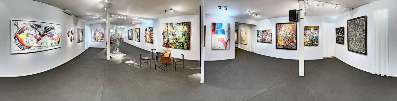 Photo panoramique de l'intérieur d'une galerie d'art avec des murs blancs et des tableaux